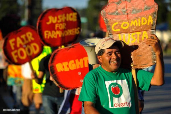 A line of protesting farm workers holding cardboard signs that say comida